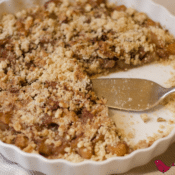 a close up of banana crumble in a white baking dish with two slices missing