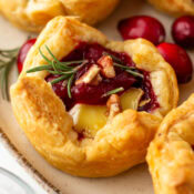 a close up of one puff pastry, cranberry, and brie appetizer bite with rosemary and pecans