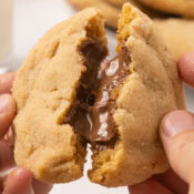 a chocolate stuffed peanut butter cookie being broken in half to reveal the gooey chocolate center