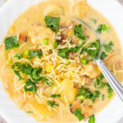 a bowl of Zuppa Toscana - Creamy Italian Sausage and Potato Soup with kale and Parmesan cheese with a spoon