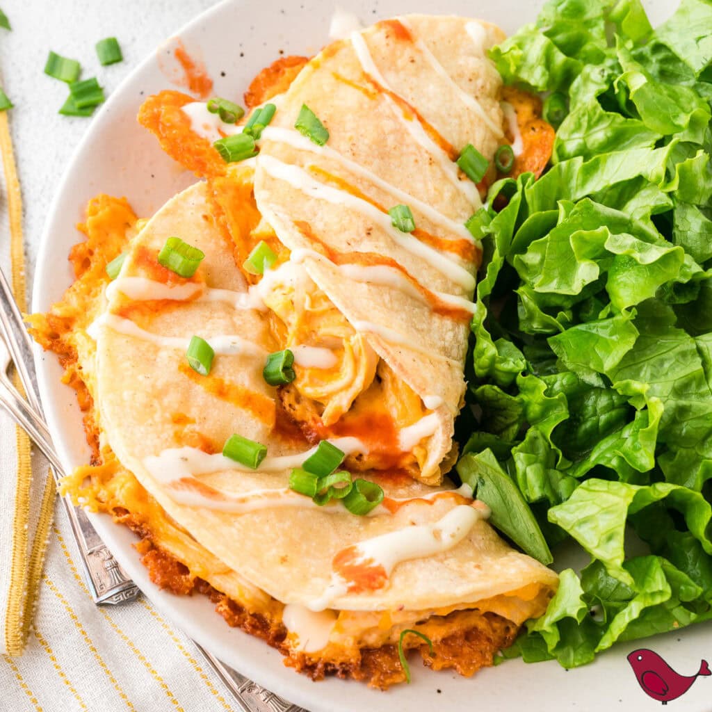 Buffalo chicken tacos drizzled with ranch on a white plate with fresh greens