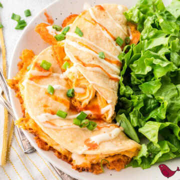 Buffalo chicken tacos drizzled with ranch on a white plate with fresh greens