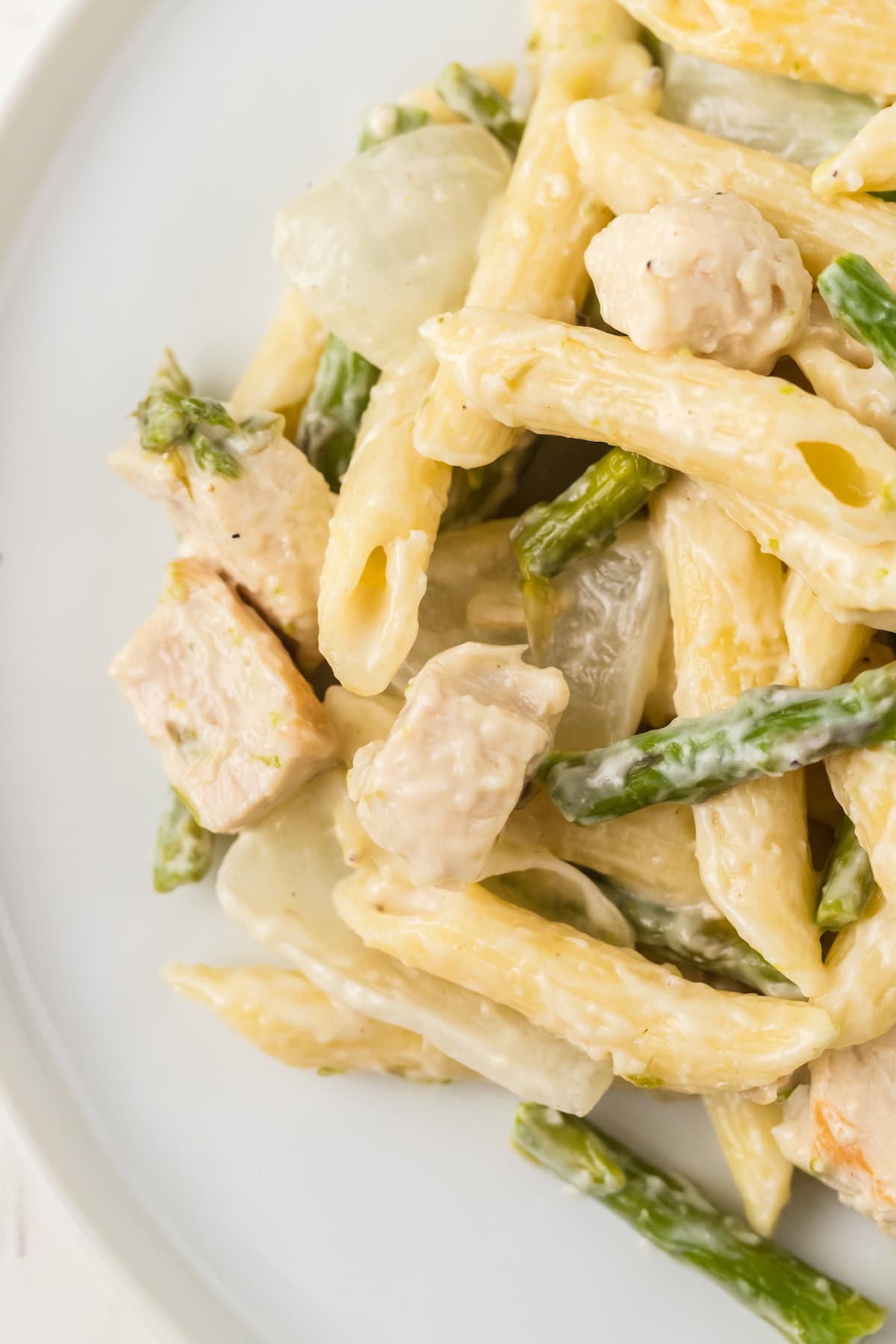 a close up of Creamy Chicken and Asparagus Pasta with alfredo sauce on a white plate