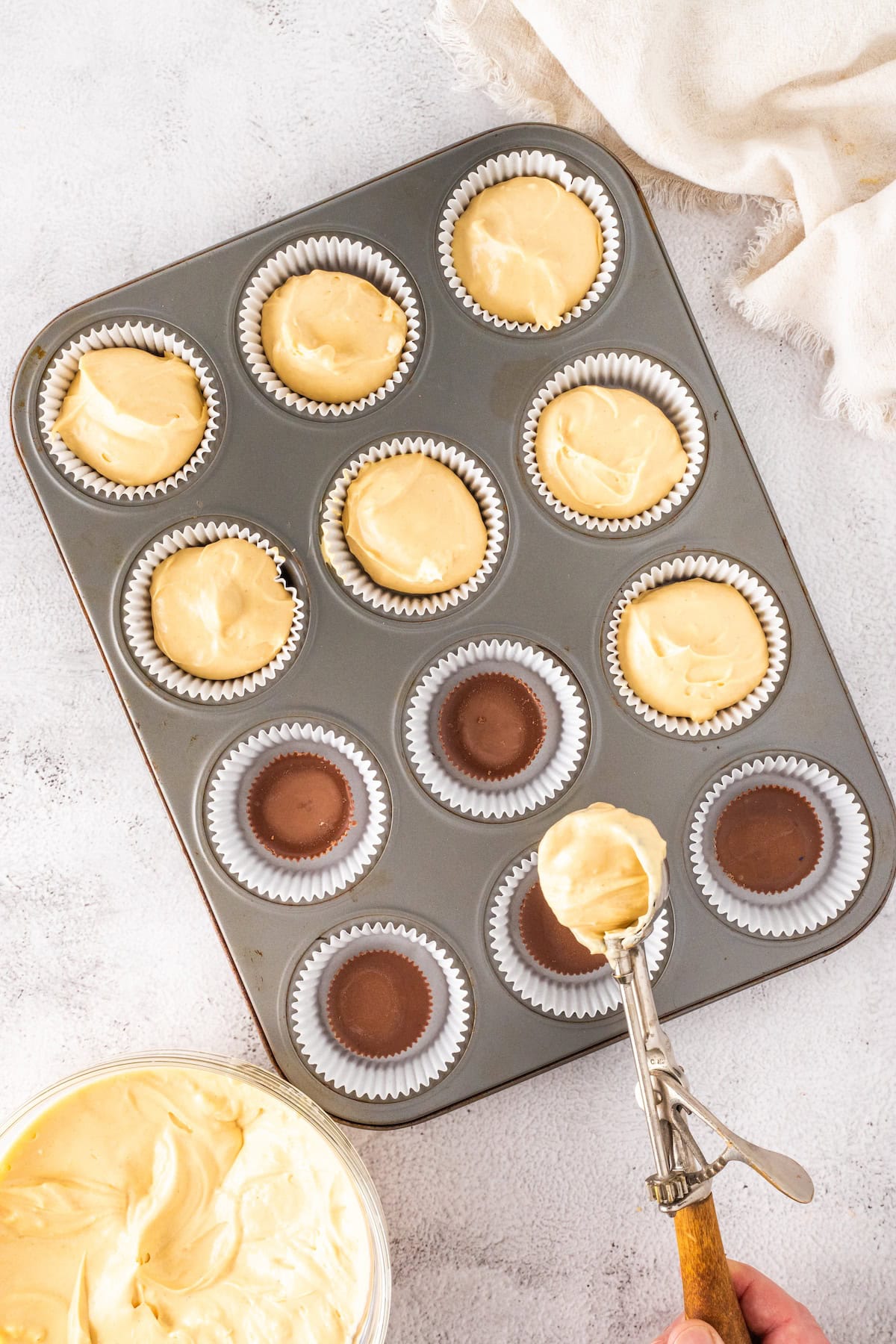 use a small scoop to distribute the peanut butter cheesecake filling among the cupcake wrappers
