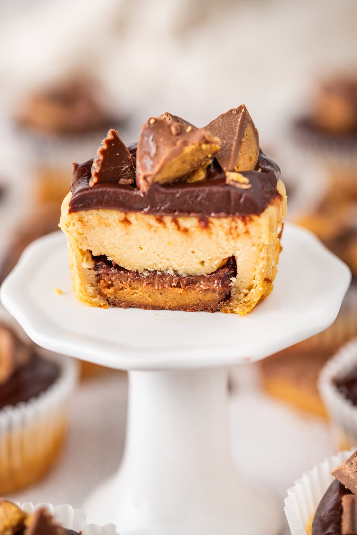 one Mini Peanut Butter Cup Cheesecake on a cupcake stand, cut in half to show the Reese's peanut butter cup on the bottom
