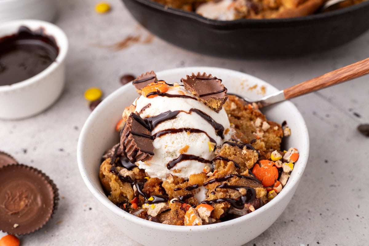 one serving of the ultimate peanut butter skillet cookie showing PB cups, Reese's Pieces, and chocolate chips with vanilla ice cream and hot fudge