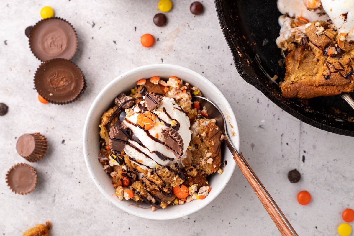 one serving of the ultimate peanut butter skillet cookie showing PB cups, Reese's Pieces, and chocolate chips with vanilla ice cream and hot fudge and a spoon