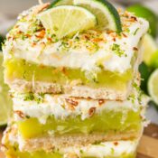 a stack of three key lime pie bars topped with key lime slices and toasted coconut
