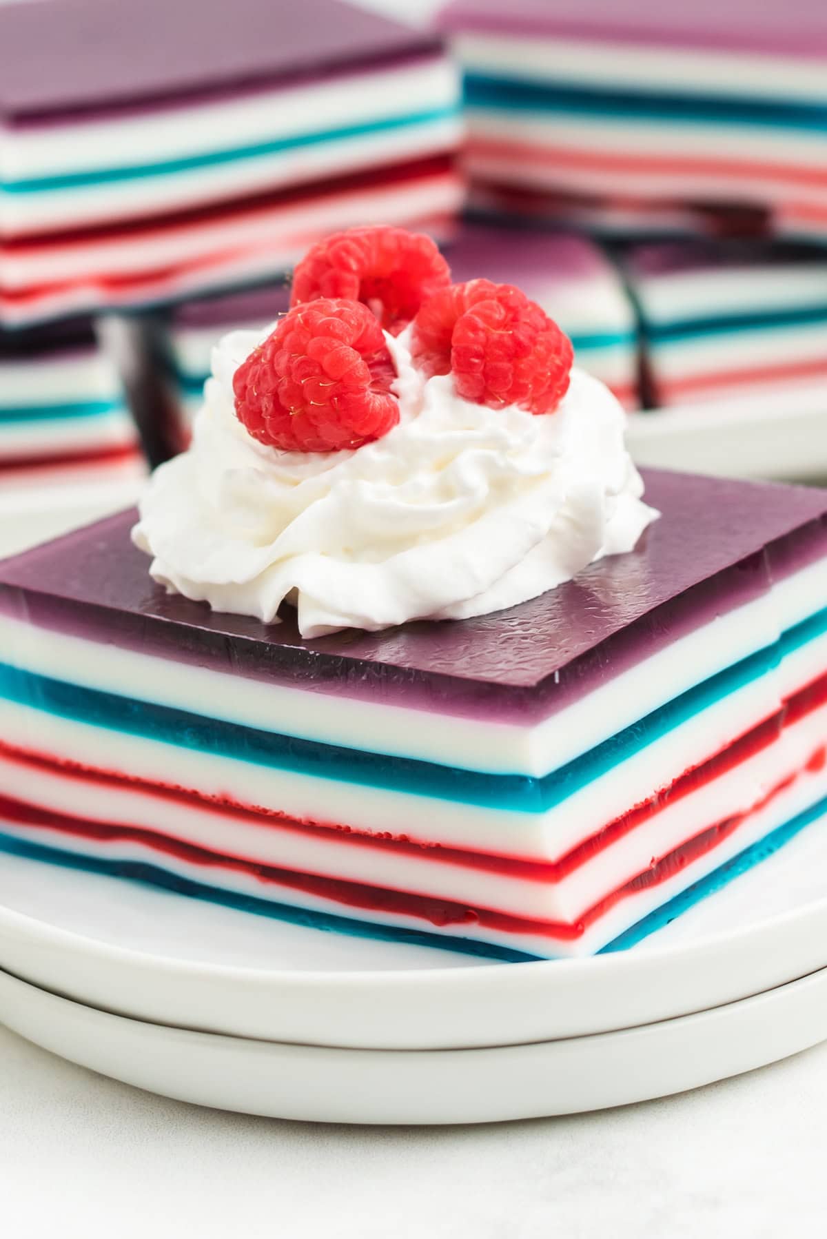 a large square of red white and blue layered jello topped with whipped cream and fresh red raspberries