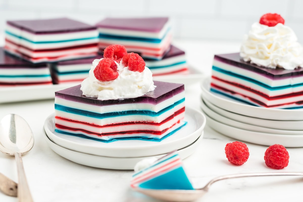 red white and blue layered jello topped with whipped cream and fresh red raspberries and a spoon