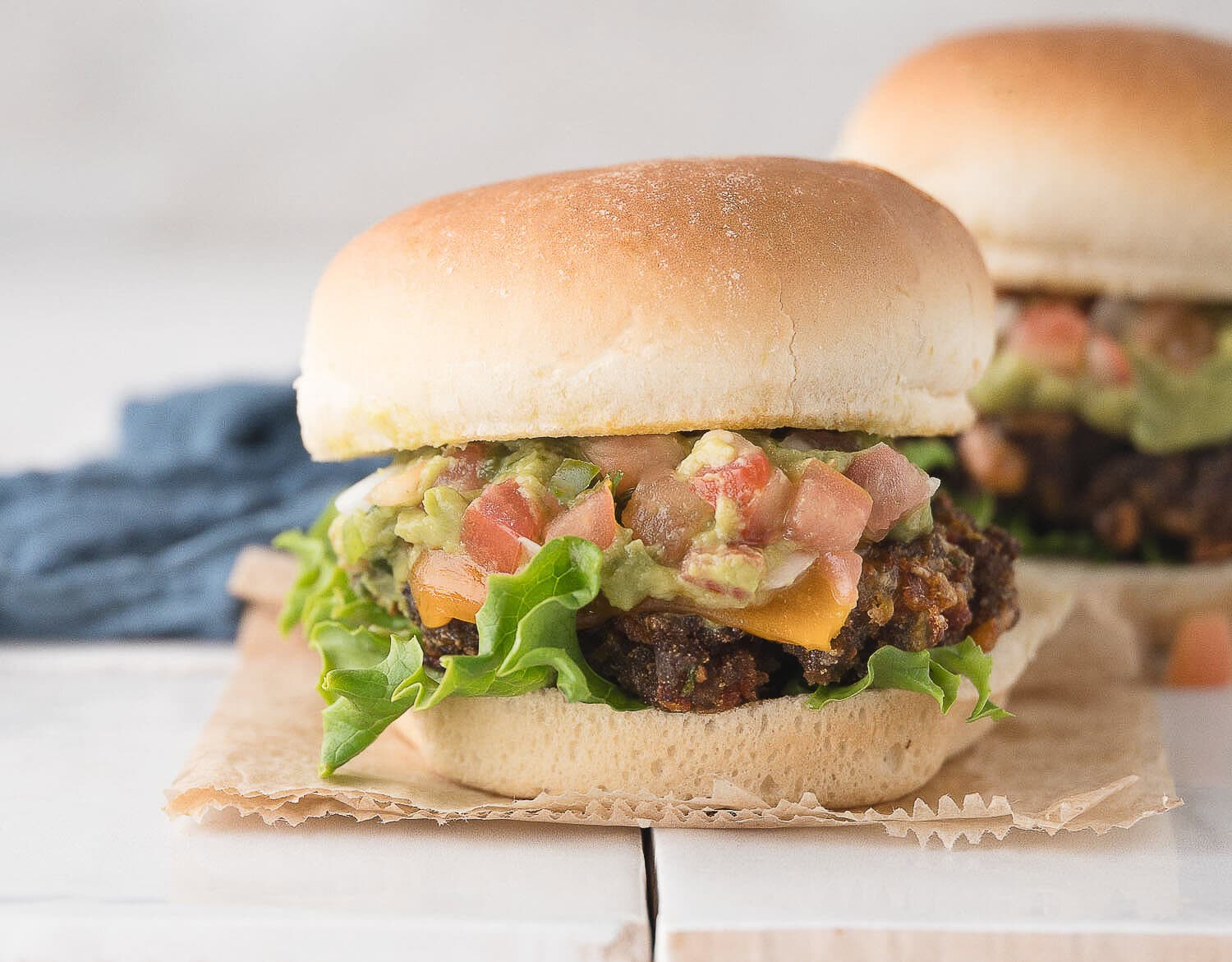 one taco burger with lettuce, salsa, guacamole, and cheddar cheese on a tall bun after being cooked in the air fryer