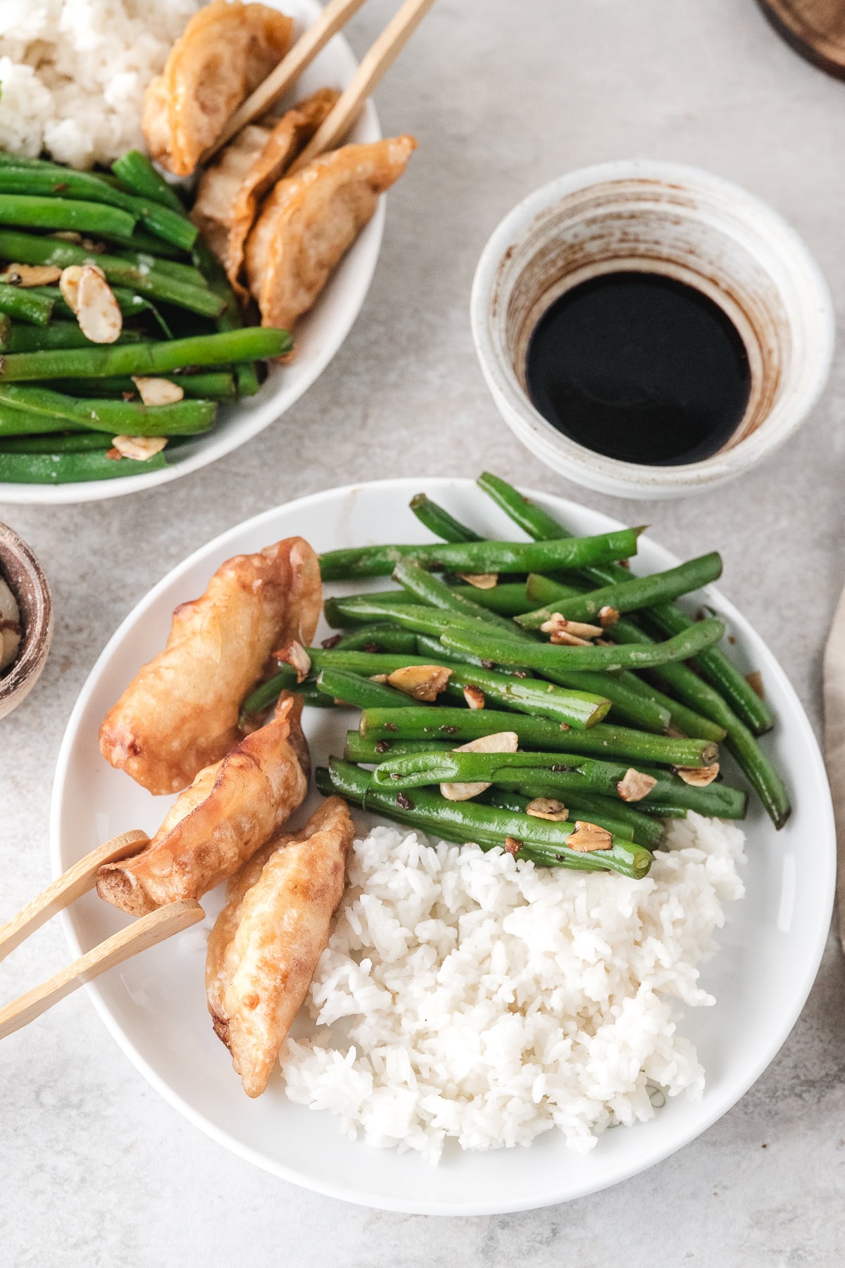 Chinese buffet green beans with pot stickers and white rice on white plates with soy sauce