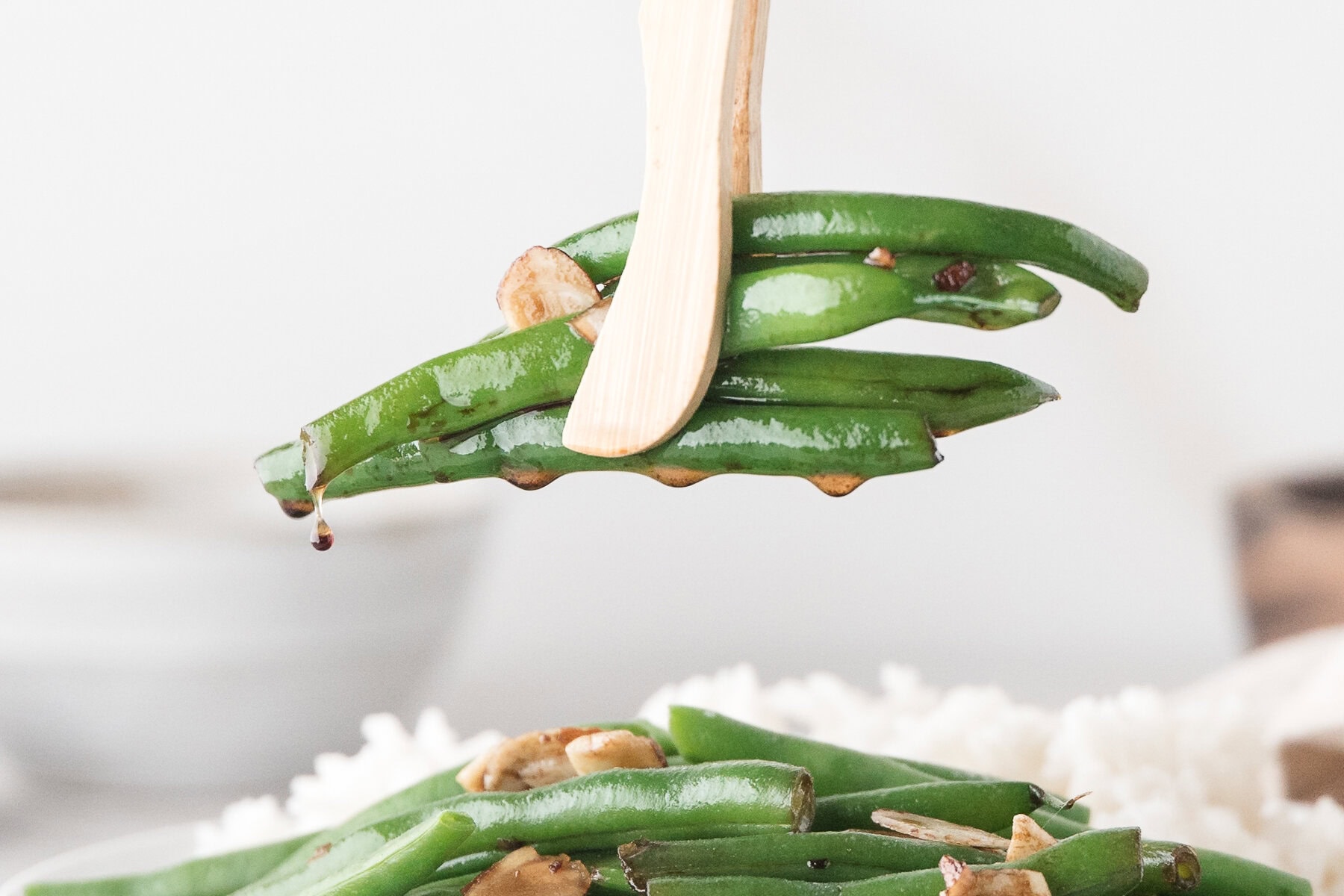 Asian Green Beans in tongs with the sesame soy sauce dripping off
