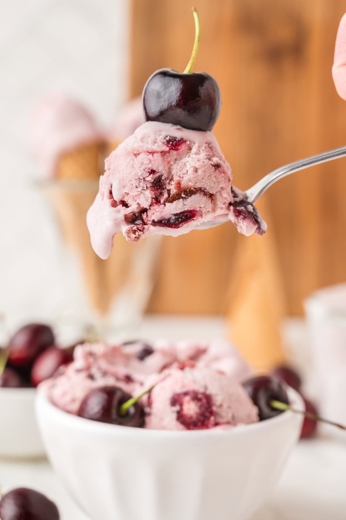 one spoonful of homemade cherry ice cream topped with a fresh black cherry