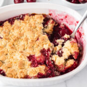 easy cherry cobbler with fresh cherries and a golden crust in a white baking dish with a serving spoon