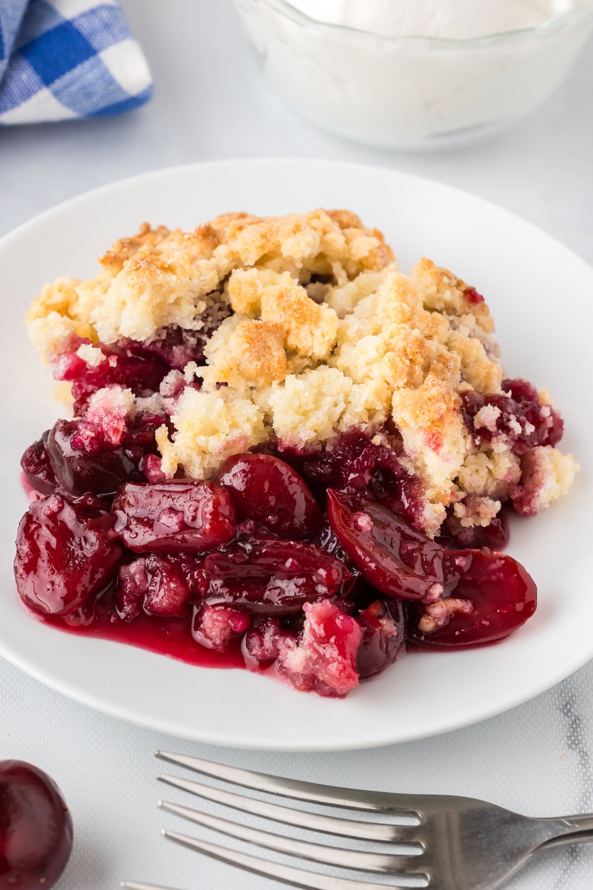 a close up of one serving of easy cherry cobbler with fresh cherries on a white plate with a fork