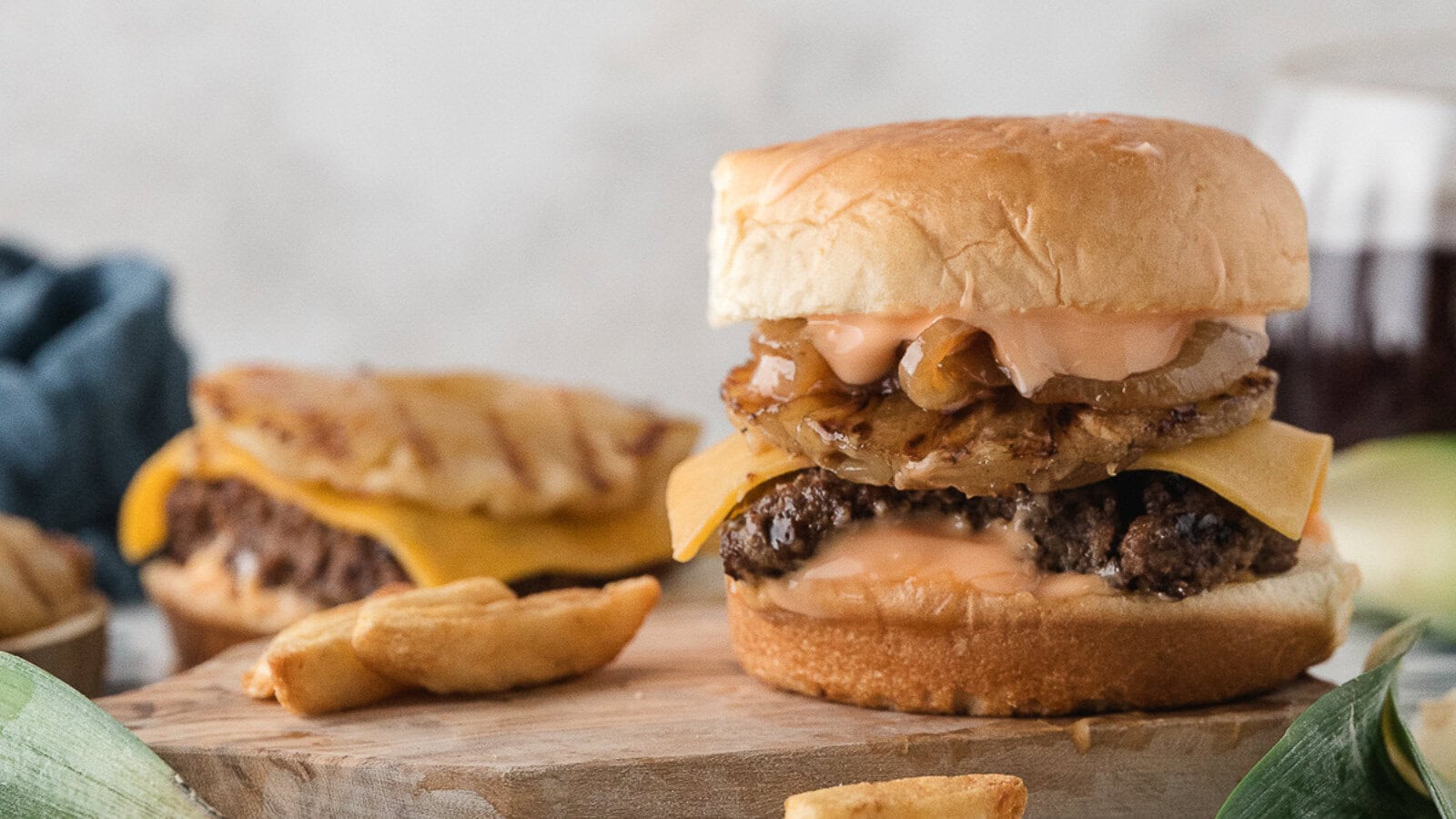 Hawaiian burgers on the stove topped with caramelized onions, grilled pineapple, melted cheese, and sweet and sour aioli on a sweet Hawaiian roll