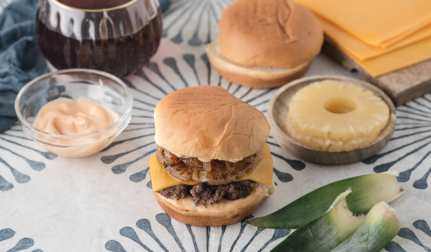 a Hawaiian pineapple burger on a Hawaiian roll with pineapple and aioli in the background