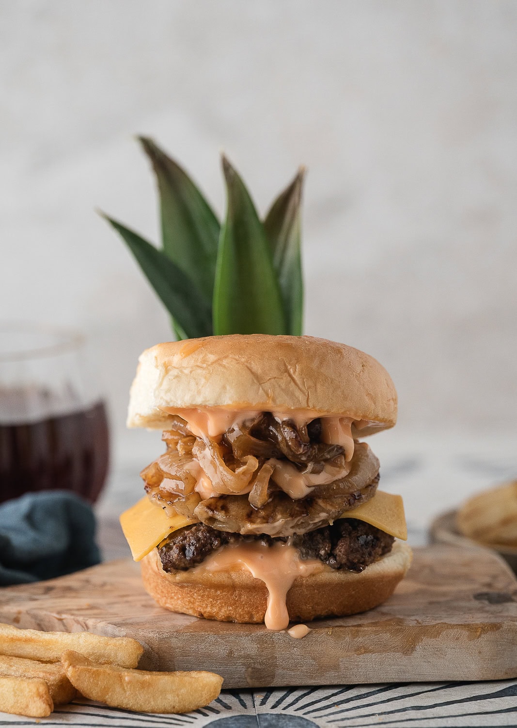 a tall burger with caramelized onions, grilled pineapple, cheddar cheese, and sweet and sour mayo on a Hawaiian roll