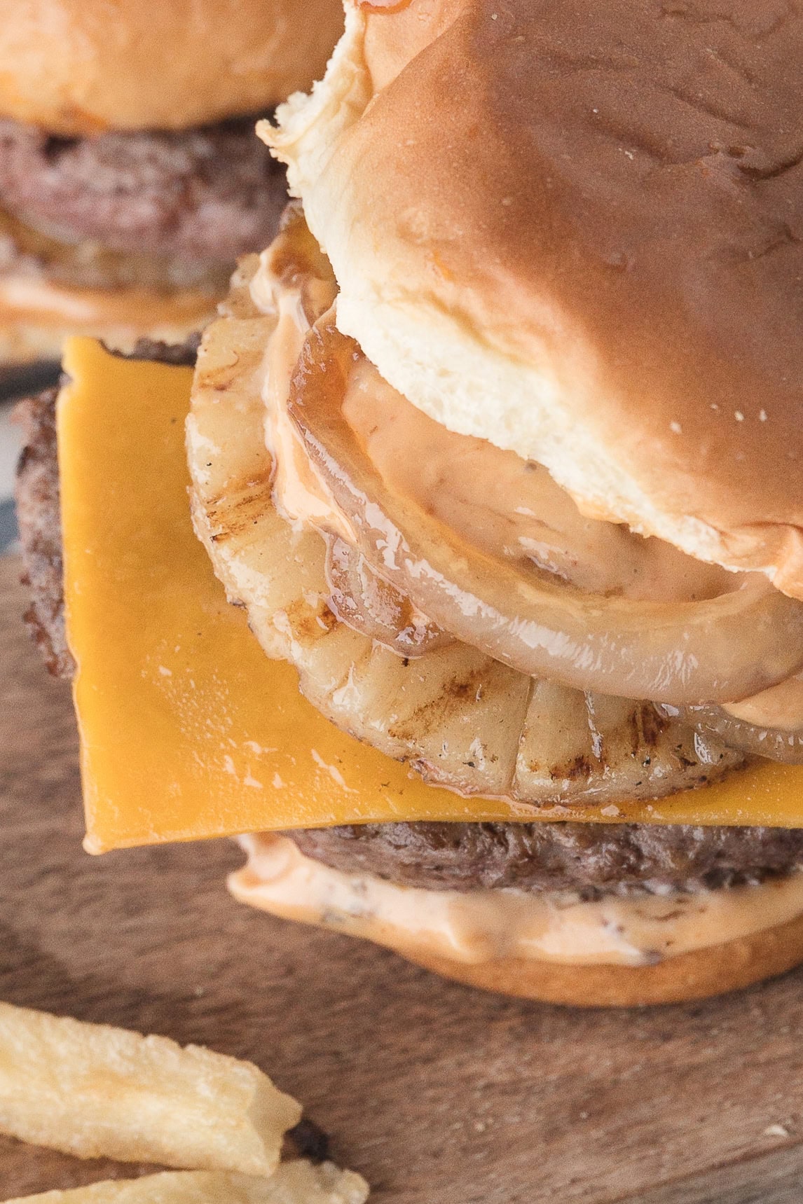 a Hawaiian burger topped with cheddar cheese, grilled pineapple, cooked onions, and sweet and sour mayo with a Hawaiian roll