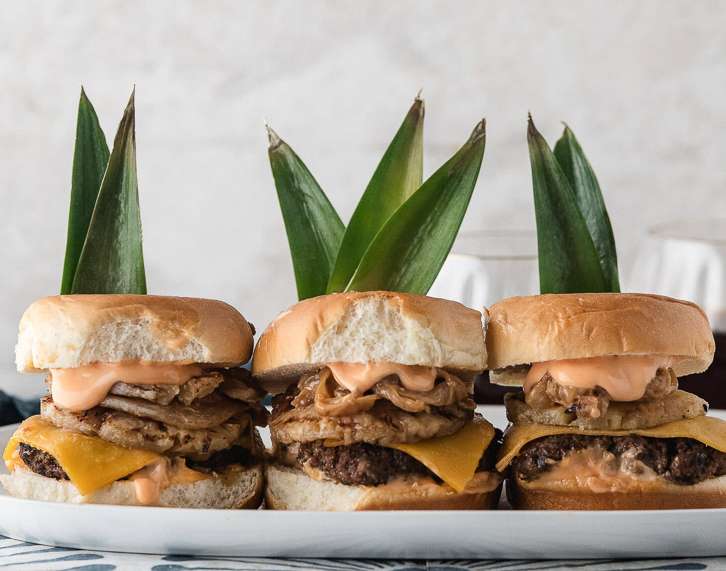 three stove top burgers topped with grilled pineapple, cheddar cheese, and sweet onions with Hawaiian rolls