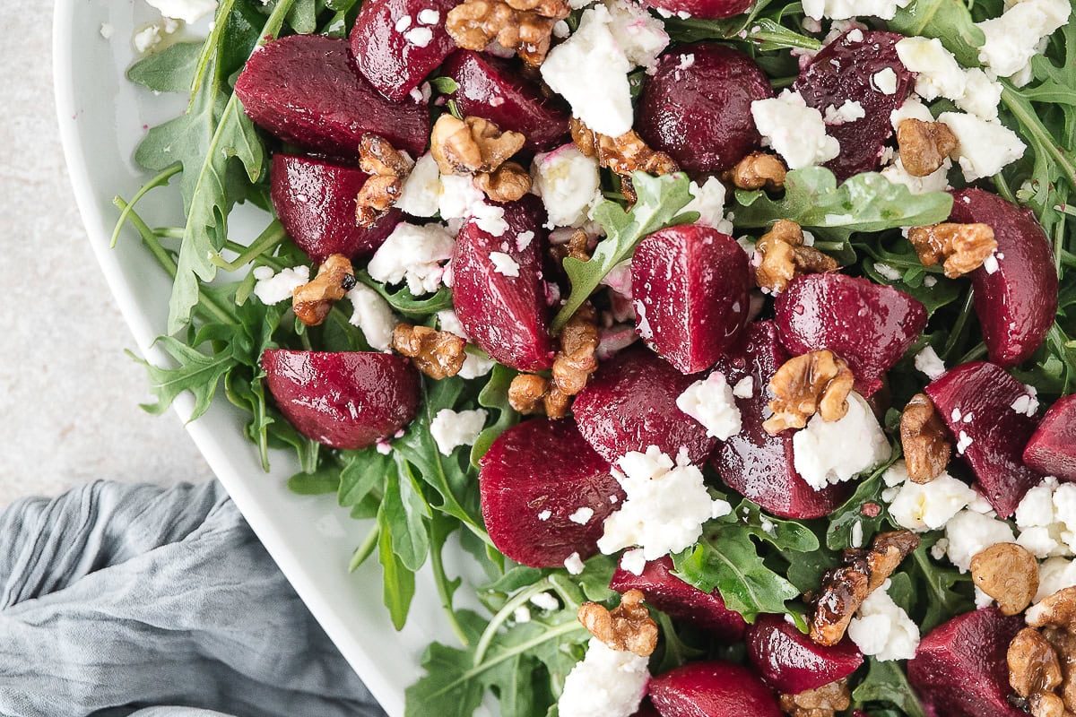 a close up of roasted beet salad with feta, arugula, and walnuts