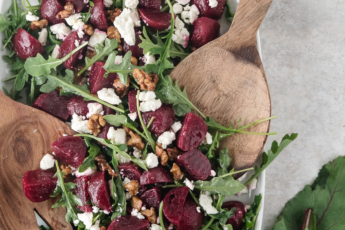 roasted beet and feta salad with arugula and walnuts with serving tongs