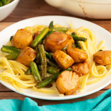 Scallops and pasta with asparagus in a white wine garlic butter sauce on a white plate