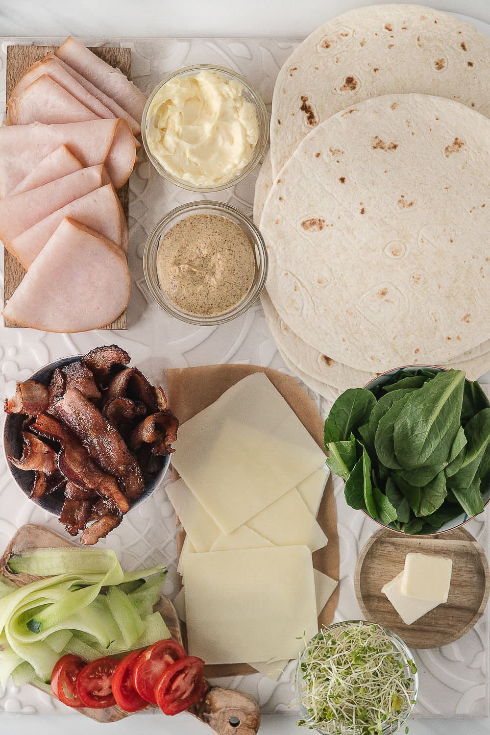 turkey bacon wrap ingredients including tortillas, mozzarella cheese, deli turkey, bacon, cucumbers, spinach, tomatoes, and bean sprouts