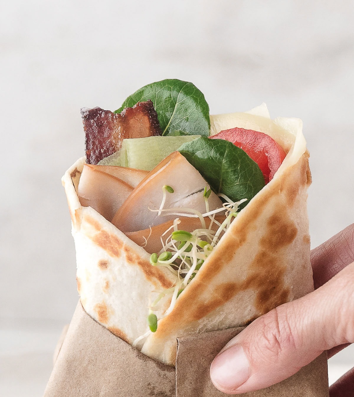 one turkey club wrap with bacon held in a napkin