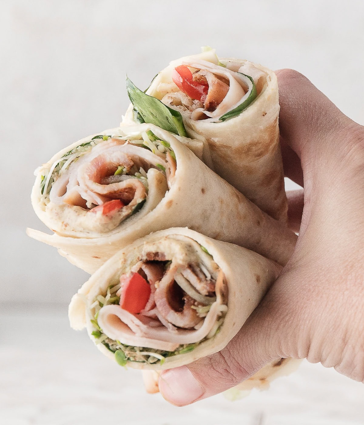 three turkey club wraps with bacon with a hand