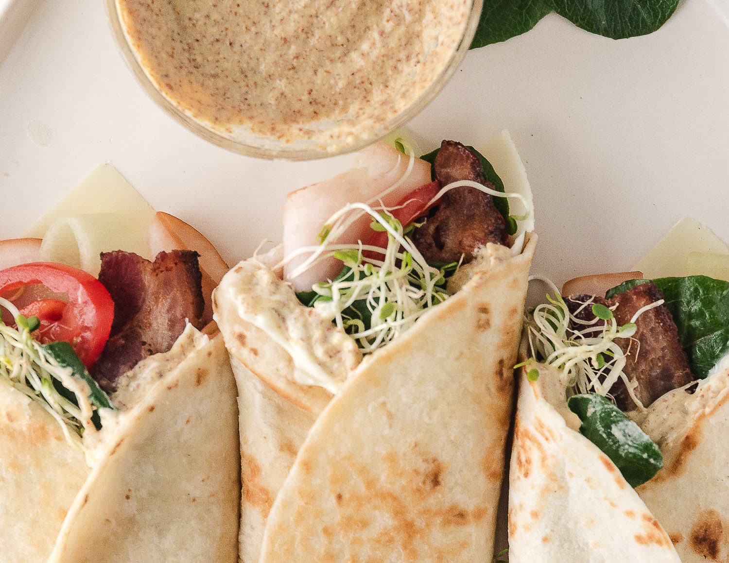 three turkey bacon wraps on a plate with mustard
