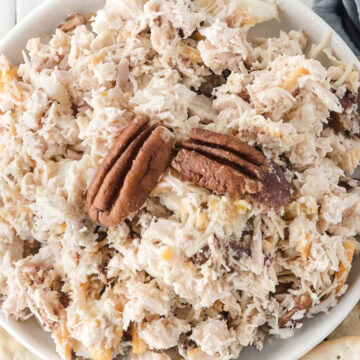 a white bowl full of canned chicken salad and topped with two pecan halves