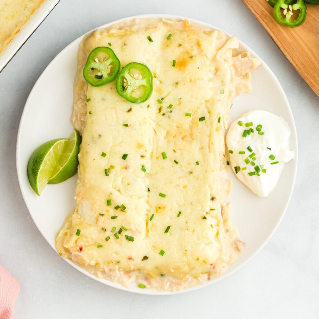 two easy white chicken enchiladas on a white plate with lime wedges and sour cream