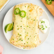 two easy white chicken enchiladas on a white plate with lime wedges and sour cream