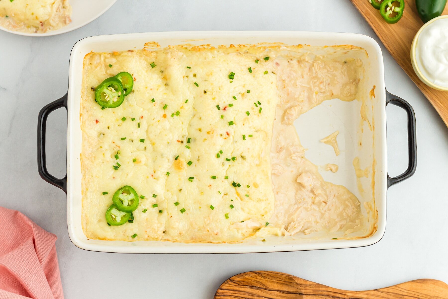 a pan of Creamy White Chicken Enchiladas with two enchiladas removed and cream of chicken sauce spilling out