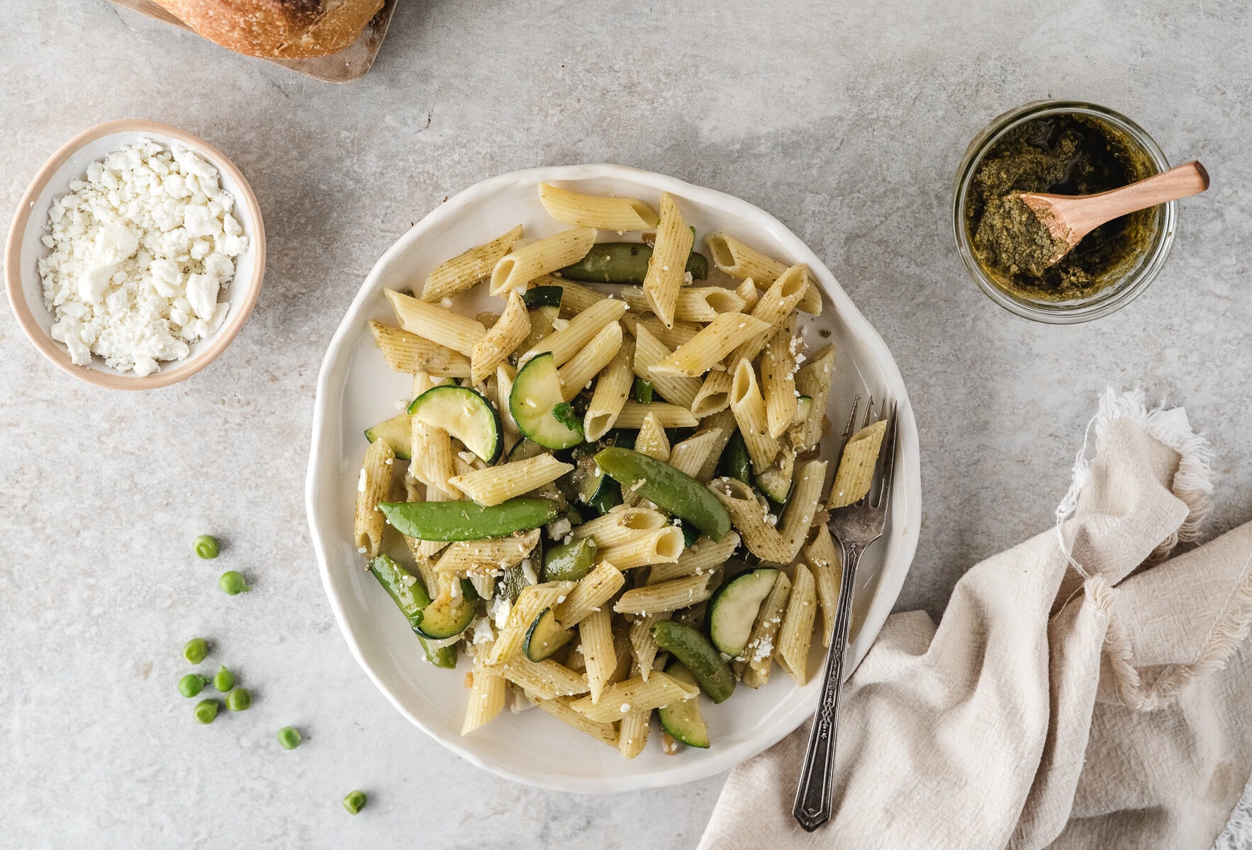 easy pasta primavera on a white plate with pesto in a jar