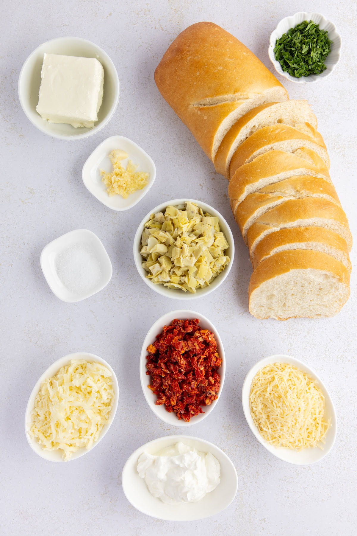 Artichoke Bruschetta with Sun-Dried Tomatoes ingredients including French bread, artichokes, sun-dried tomatoes, fresh garlic, Parmesan cheese, mozzarella cheese, cream cheese, and sour cream