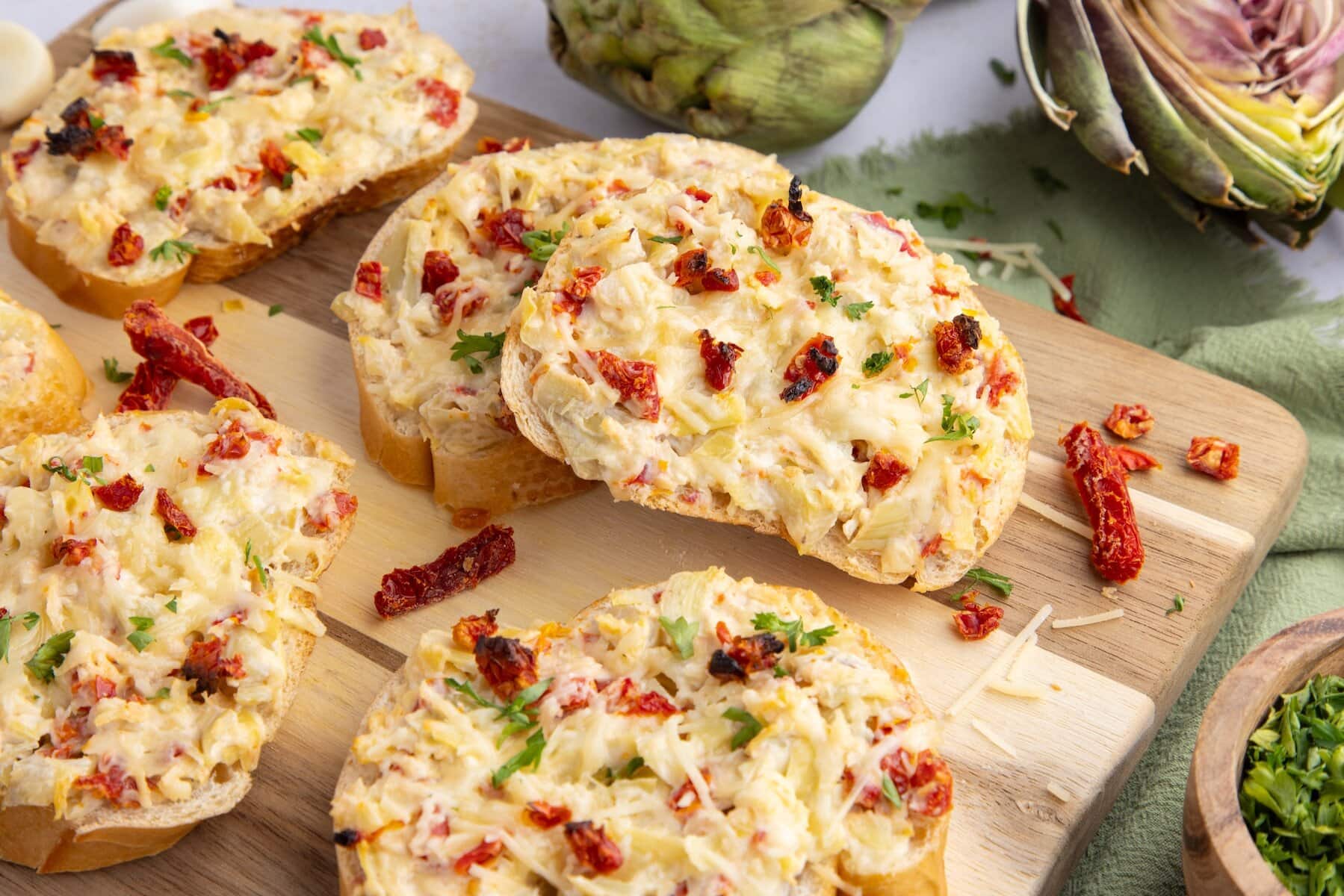 several slices of Artichoke Bruschetta with Sun-Dried Tomatoes on a cutting board with Parmesan cheese