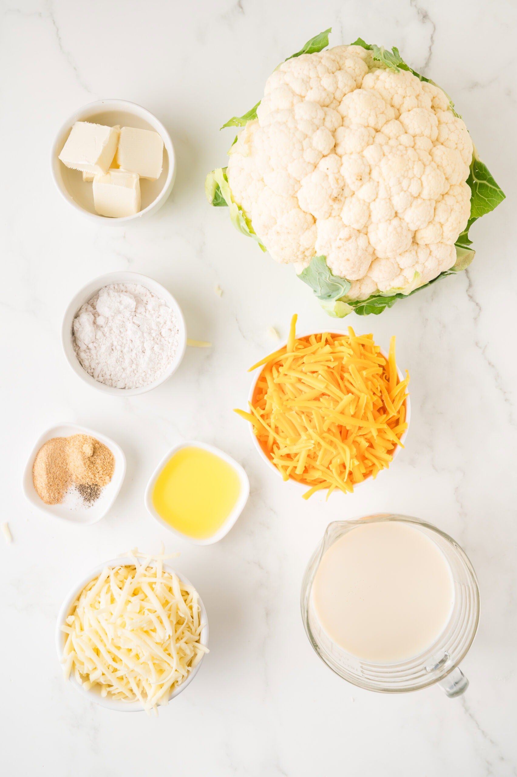All Ingredients (flour, shredded cheese, melted butter, spices, cauliflower) pictured ready to make cauliflower mac & cheese