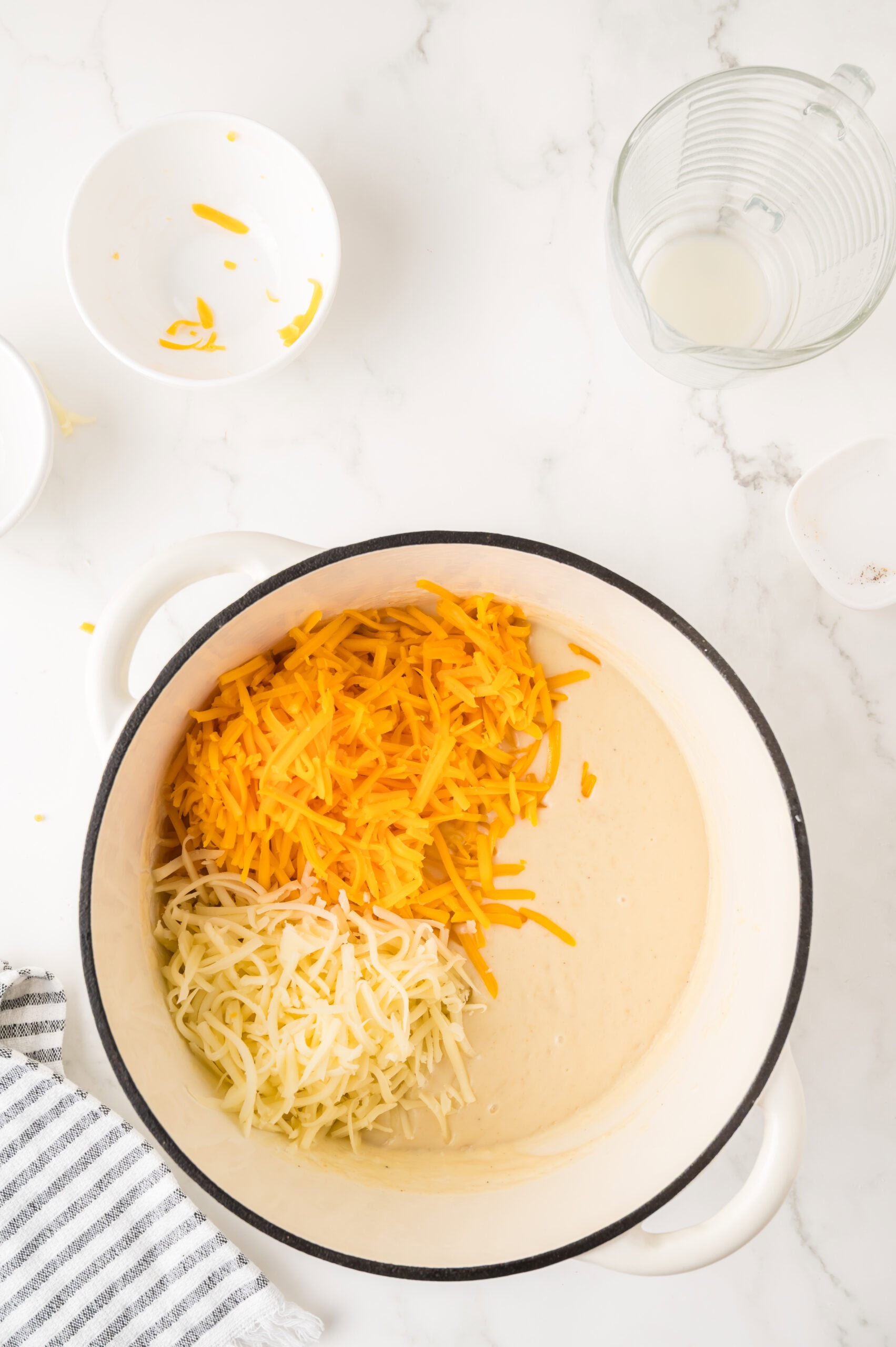 The cheeses being added to the melted butter and flour to create the cheese sauce for cauliflower mac & cheese