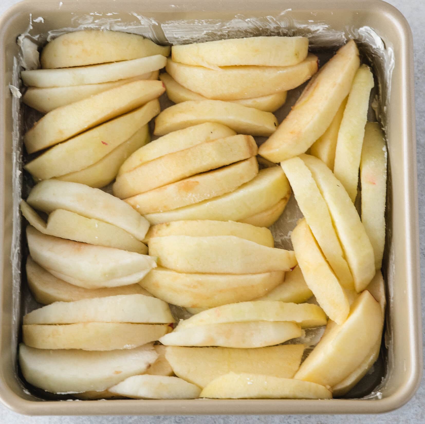 apples are cored and peeled in a buttered pan ready to add the dry ingredients on top to finish this recipe and bake