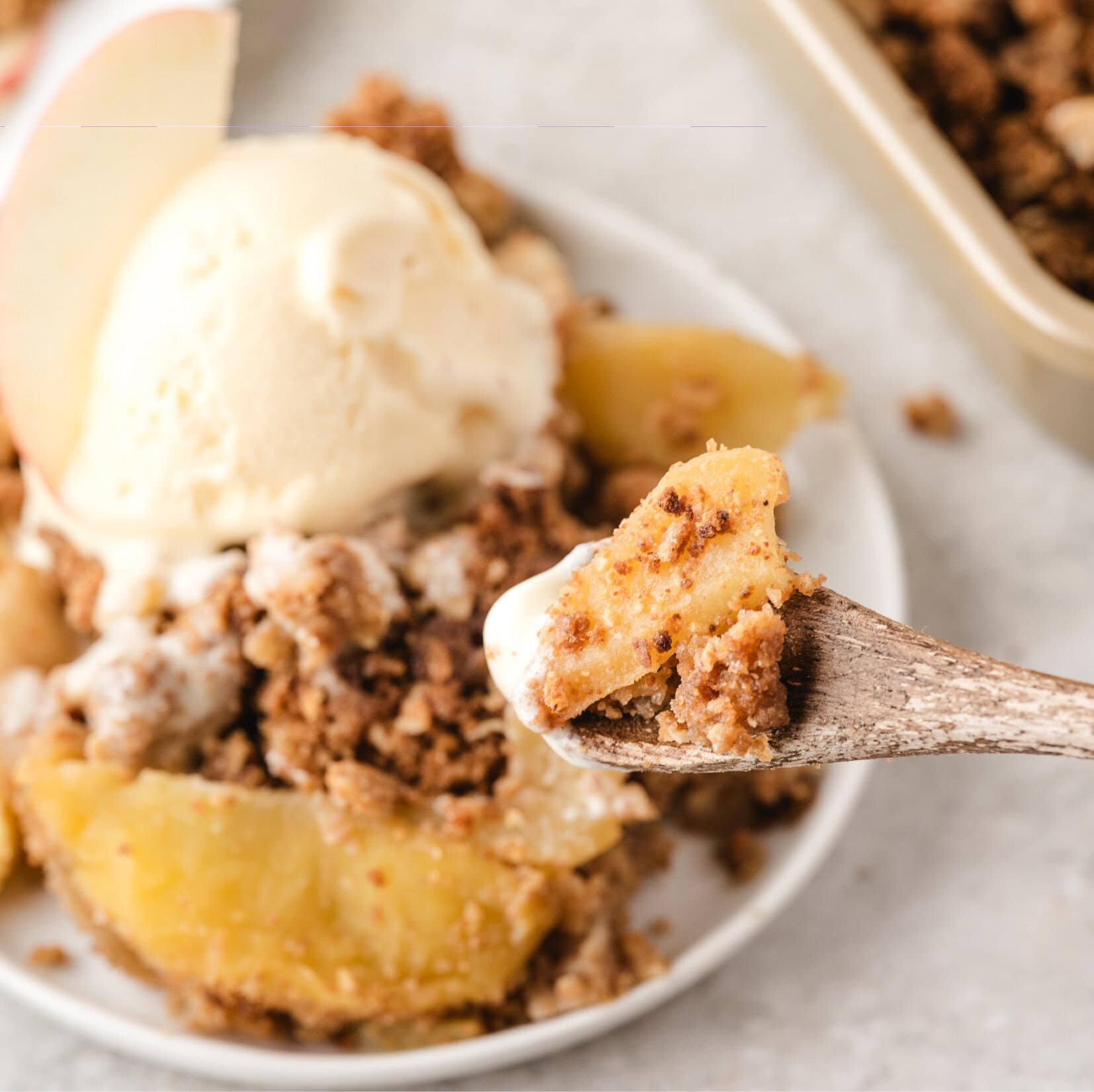 apple crisp with oats and graham cracker plated in a small dish with a scoop of vanilla ice cream showing a spoonful closely
