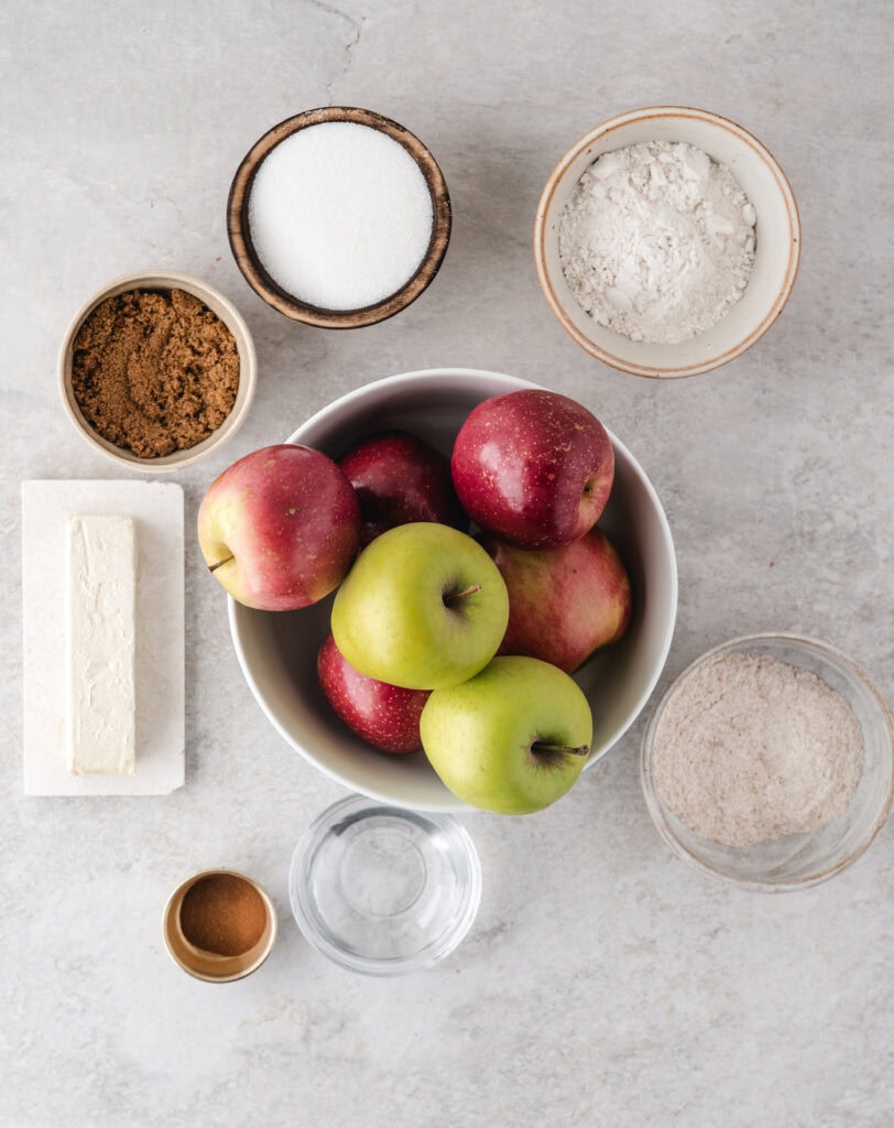 In this healthy Apple Crisp without Oats recipe is the ingredients pictured. The ingredients are different types of apples (six,) cinnamon spice, water, one stick of butter, white and brown sugar, all-purpose flour and whole wheat flour