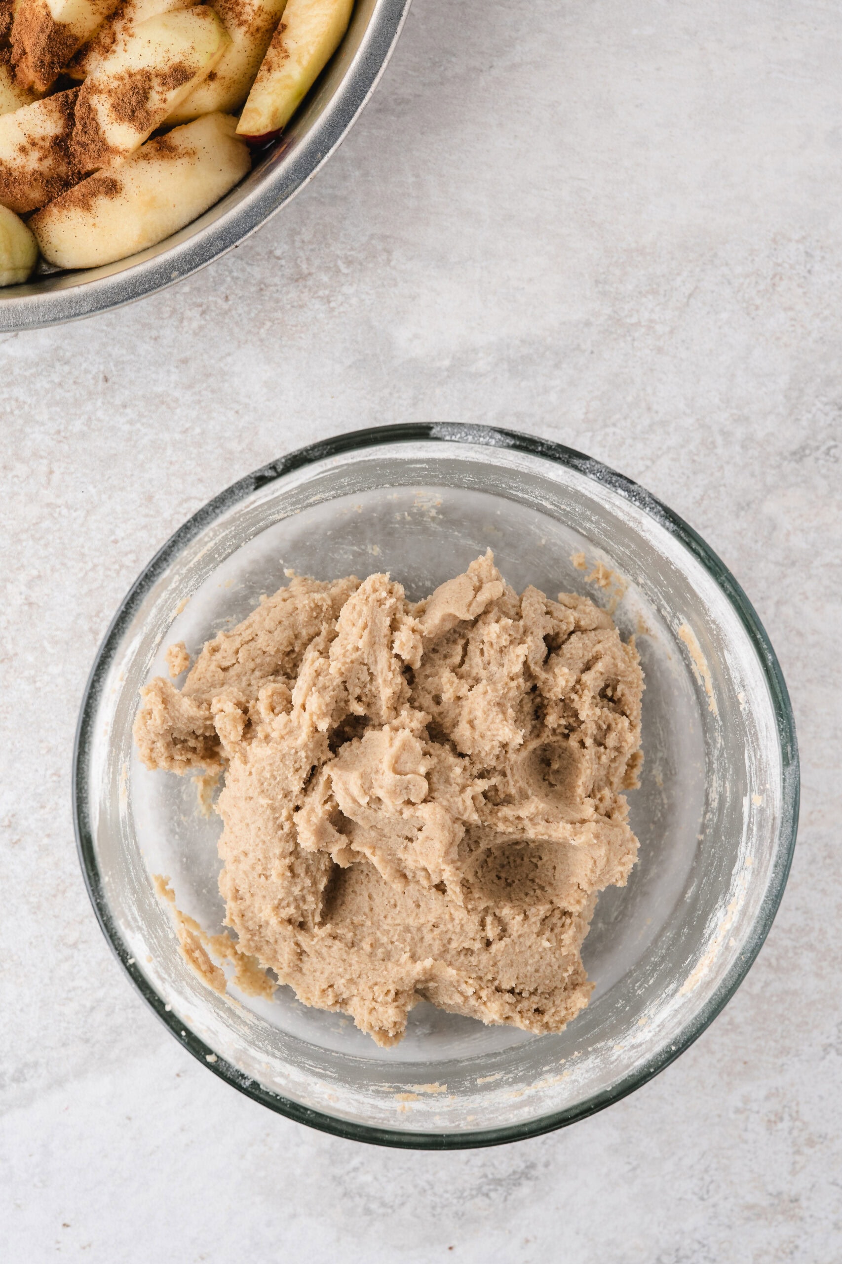 In this quick Apple Crisp without Oats is the dough all mixed and ready to be placed on top of apples. It has a paste-like consistency. In the upper left hand corner is apples cored, and peeled ready for the dough .