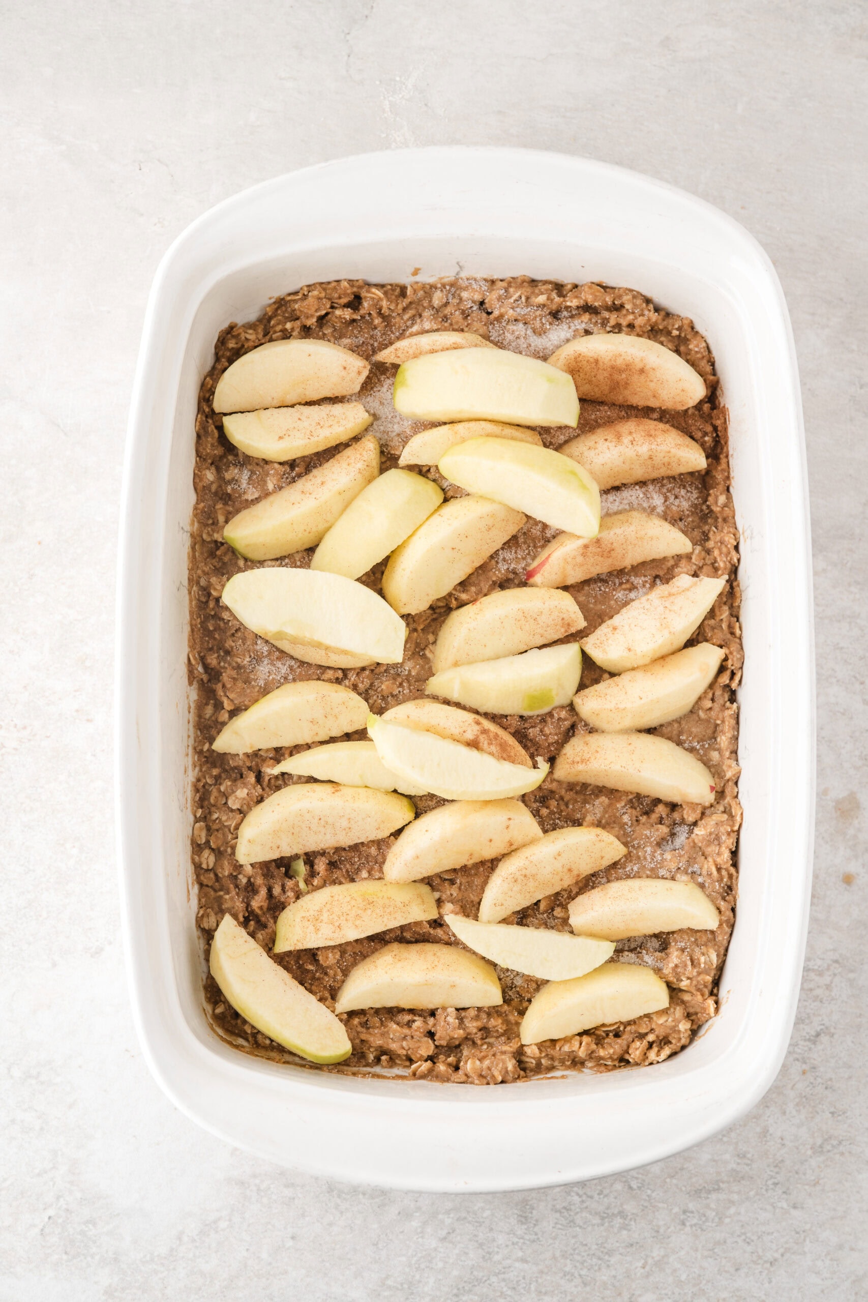 Easy apple crisp showing the next process shot which is apples peeled, cored, and sliced on top of oat mixture that is bottom of pan
