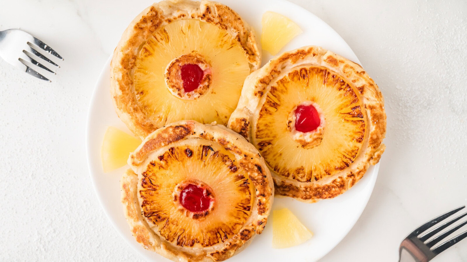 3 pineapple upside down pancakes on a white plate surrounded by pineapple chunks
