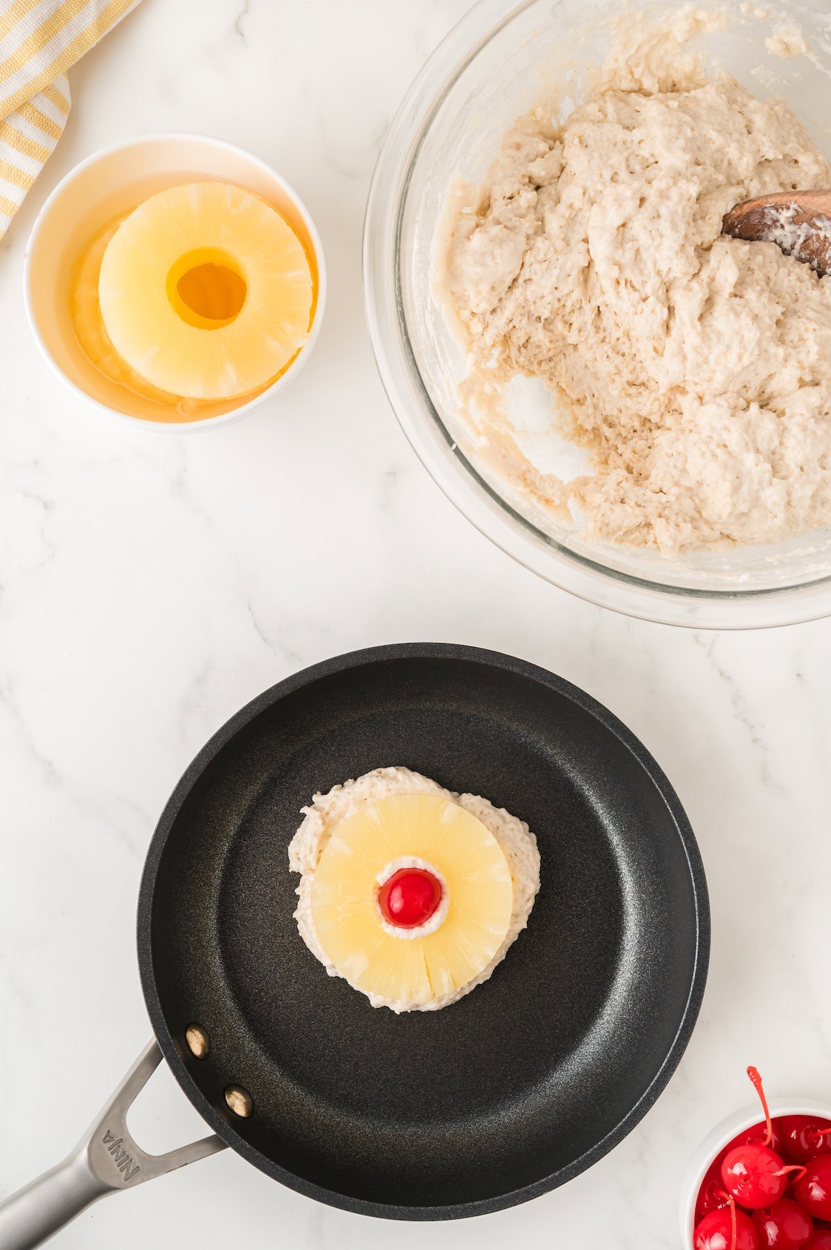 pour a scoop of batter onto a skillet and top with a pineapple ring and a maraschino cherry