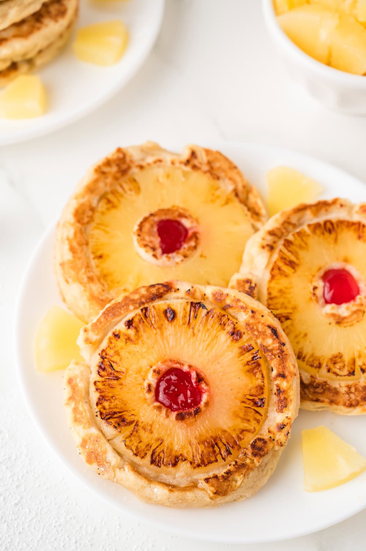 three pineapple upside down pancakes with pineapple chunks on a white plate