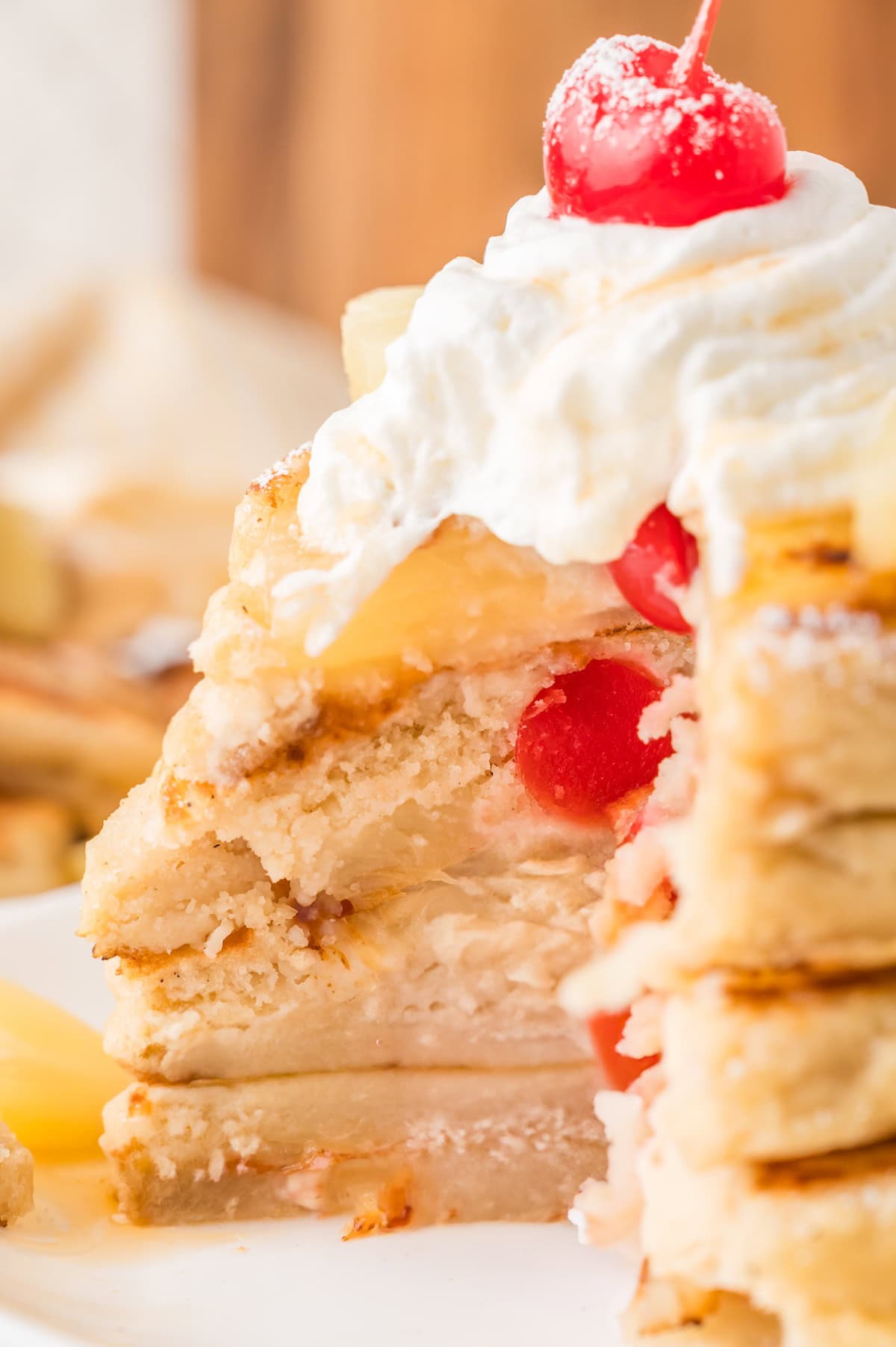 a stack of pineapple upside down pancakes with a slice cut away, showing the pineapple slices and cherries stuffed inside the pancakes